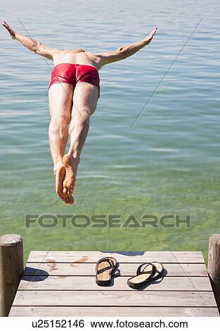 Stock Photograph - Man in swimsuit jumping into lake. Fotosearch
