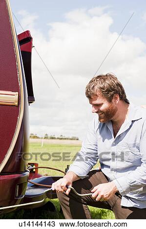 Stock Image - Man working on trailer in field. Fotosearch
