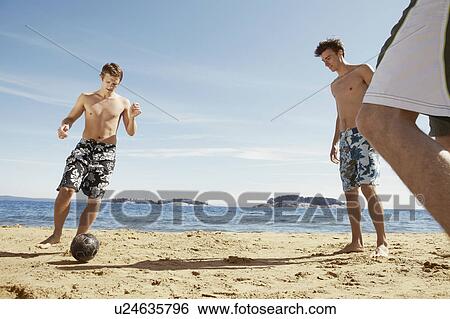 Stock Photograph - Men playing soccer on beach. Fotosearch