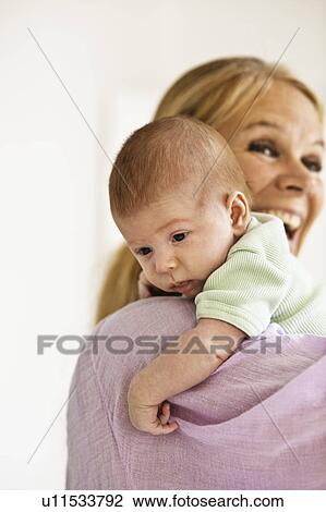 Stock Image - Mother cradling infant on shoulder. Fotosearch