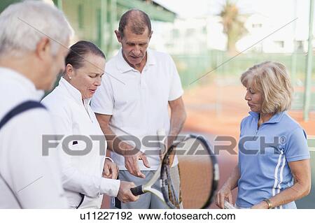 Stock Image - Older couples talking on tennis court. Fotosearch