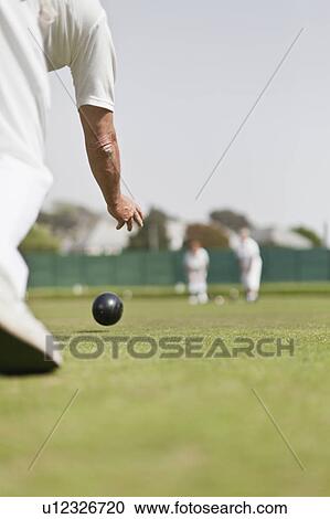 Stock Image - Older man lawn bowling. Fotosearch