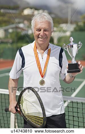 Stock Image - Older man with trophy on tennis court. Fotosearch