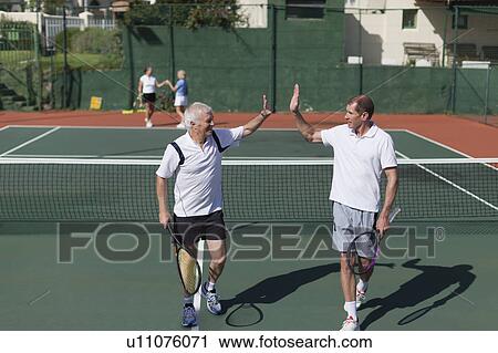 Stock Image - Older men high-fiving on tennis court. Fotosearch