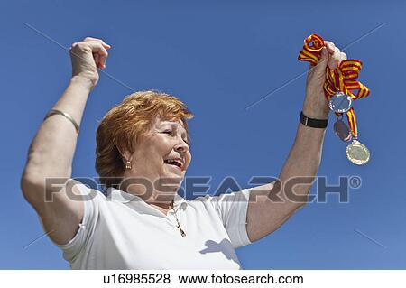 Stock Photo - Older woman cheering with medals. Fotosearch