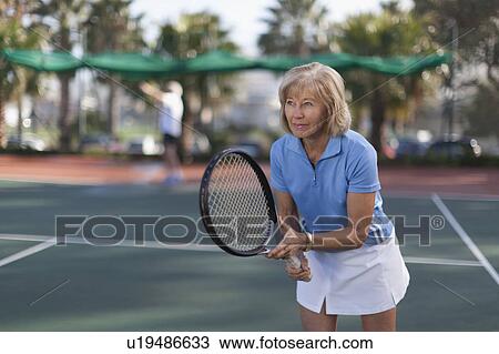 Stock Image - Older woman playing tennis outdoors. Fotosearch
