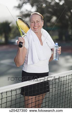 Stock Image - Older woman standing on tennis court. Fotosearch