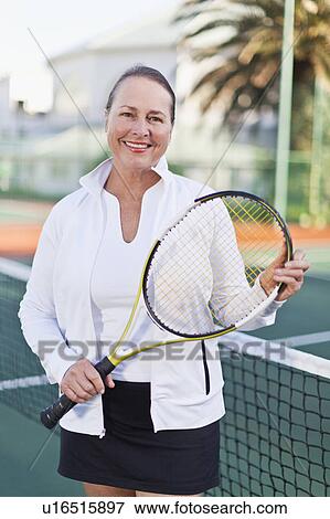 Stock Photo - Older woman with tennis racket on court. Fotosearch