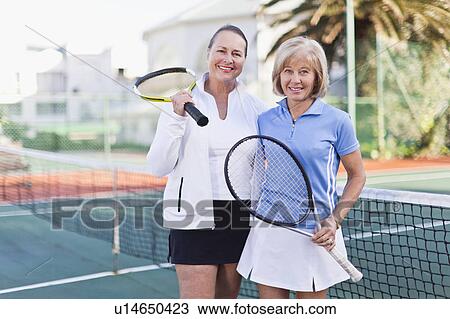 Stock Image - Older women with tennis rackets on court. Fotosearch