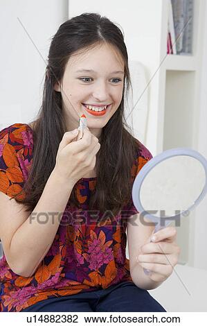 Stock Image - Smiling girl applying lipstick in mirror. Fotosearch
