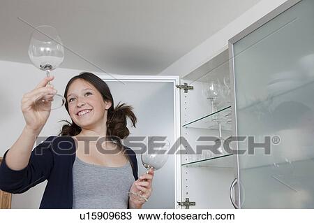 Stock Image - Smiling girl putting away wine glasses. Fotosearch