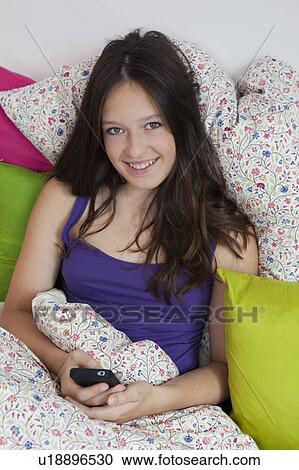 Smiling girl using cell phone in bed View Large Photo Image Stock Image - Smiling girl using cell phone in bed. Fotosearch
