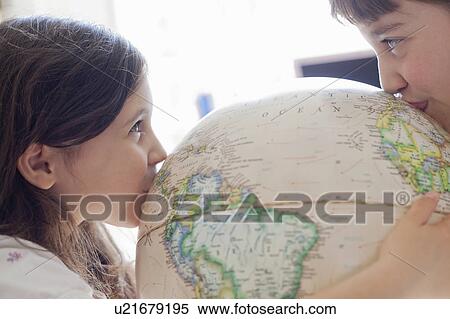 Stock Photography - Smiling girls kissing globe indoors. Fotosearch