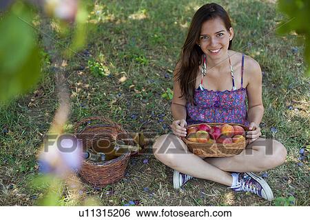 Stock Photograph - Smiling woman picnicking in orchard. Fotosearch