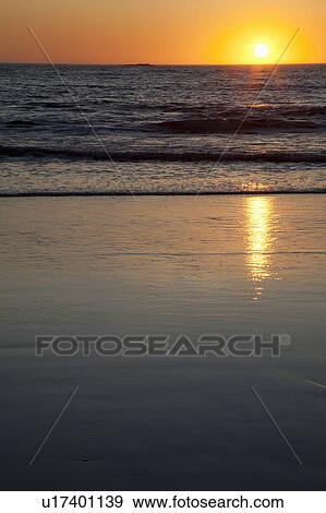 Stock Photo - Sun setting over ocean on beach. Fotosearch