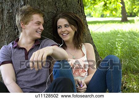 Stock Image - Teenage couple sitting together in park. Fotosearch