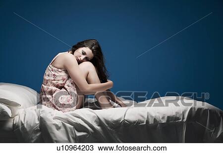 Stock Image - Teenage girl crouching on bed. Fotosearch