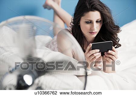 Stock Image - Teenage girl using cell phone on bed. Fotosearch