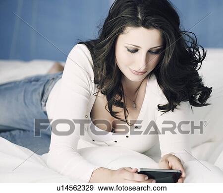 Stock Photo - Teenage girl using cell phone on bed. Fotosearch