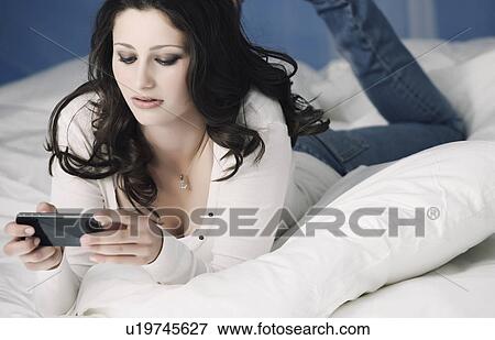 Stock Photo - Teenage girl using cell phone on bed. Fotosearch