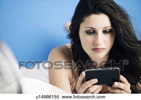 Stock Photography - Teenage girl using cell phone on bed. Fotosearch