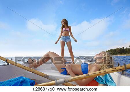 Stock Image - Teenage girls relaxing on sailboat. Fotosearch