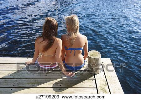 Stock Photo - Teenage girls relaxing on wooden pier. Fotosearch
