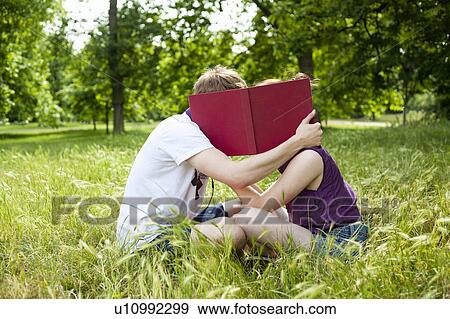 Stock Photo - Teenagers hiding behind book in park. Fotosearch