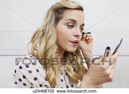 Stock Image - Woman applying mascara in mirror. Fotosearch