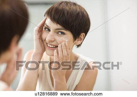 Woman applying moisturizer in mirror View Large Photo Image Stock Photo - Woman applying moisturizer in mirror. Fotosearch
