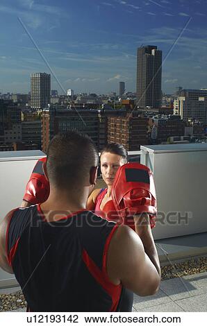 Stock Image - Woman boxing with coach on rooftop. Fotosearch