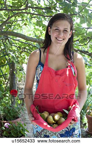 Stock Image - Woman carrying fruit in apron outdoors. Fotosearch