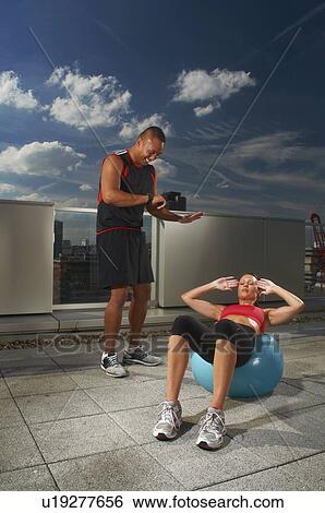 Stock Photograph - Woman exercising with trainer on rooftop. Fotosearch