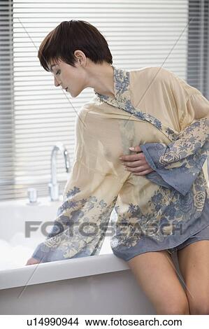 Picture - Woman in robe testing bathwater. Fotosearch