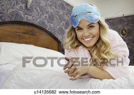 Stock Image - Woman on bed with eye mask on forehead. Fotosearch