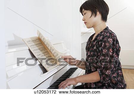 Stock Image - Woman playing piano at home. Fotosearch