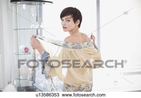 Stock Image - Woman removing sheer robe in bathroom. Fotosearch