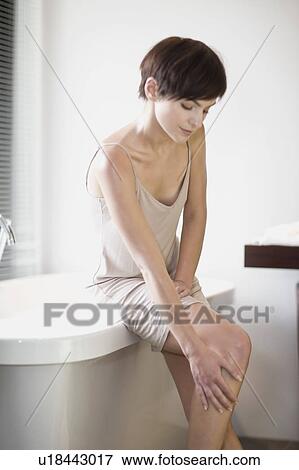 Stock Photo - Woman sitting on edge of bathtub. Fotosearch