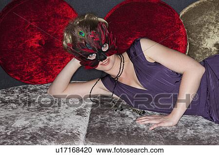Stock Image - Woman wearing feather mask in bar. Fotosearch