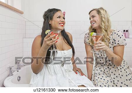 Stock Image - Women drinking martinis in bathroom. Fotosearch