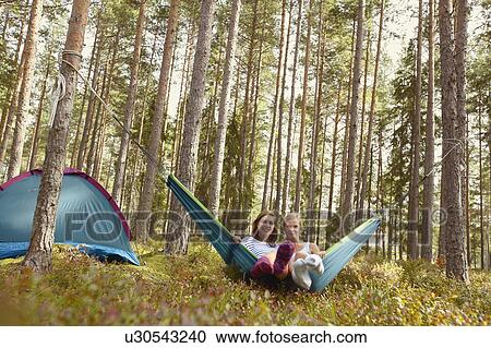 Stock Image - Women relaxing in hammock at campsite. Fotosearch