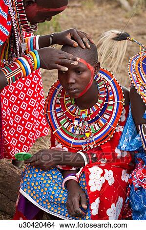 マサイ族 適用 ペンキ ために Celebrations 若い女性 服を着せられる 中に カラフルである 衣類 そして 多く ビーズ 宝石類 座る 間 赤いペイント ある 応用 へ 彼女 顔 によって もう１ つ 人 女 Amboseli Kenya 東アフリカ