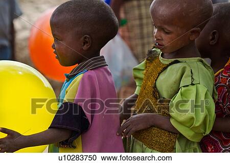 Stock Image - Close up detail of Masai children at school in conga line, with one at front holding a yellow balloon, and the one behind wishing it was hers? ÇªAmboseli, Kenya, East Africa. Fotosearch
