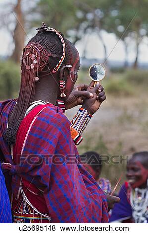 Close up side back view of young Masai warrior (moran), with long braided hair, wearing traditional red shuka and beaded jewellery, with red facial paint, checking effect in yellow plastic mirror, Amboseli, Kenya, East Africa View Large Photo Image Stock Photo - Close up side back view of young Masai warrior (moran), with long braided hair, wearing traditional red shuka and beaded jewellery, with red facial paint, checking effect in yellow plastic mirror, Amboseli, Kenya, East Africa. Fotosearch
