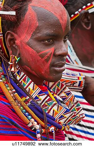 Close up side front view of young Masai warrior (moran), with long braided hair, wearing traditional red shuka and beaded jewellery, with red facial paint, Amboseli, Kenya, East Africa View Large Photo Image Stock Image - Close up side front view of young Masai warrior (moran), with long braided hair, wearing traditional red shuka and beaded jewellery, with red facial paint, Amboseli, Kenya, East Africa. Fotosearch