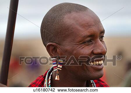 Stock Image - Close up side view of Masai warrior, wearing traditional red and blue shuka and beaded jewellery, Amboseli, Kenya, East Africa. Fotosearch