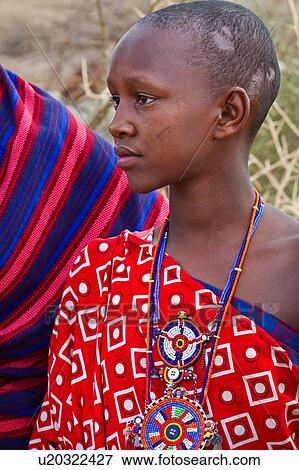 Stock Photo - Close up side view of Masai woman wearing traditional red and white cotton wrap, and beaded jewellery, acacia thorn fence in background, Amboseli, Kenya, East Africa. Fotosearch