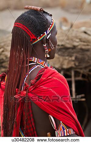 Stock Photo - Close up side view of young Masai warrior (moran), with long braided hair, wearing traditional red shuka and beaded jewellery, Amboseli, Kenya, East Africa. Fotosearch