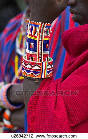 Detail of Masai warrior, wearing traditional red shuka, standing with forearm vertical to display beaded jewellery, and a background of another warrior dressed in vertical striped shuka, Amboseli, Kenya, East Africa View Large Photo Image Stock Image - Detail of Masai warrior, wearing traditional red shuka, standing with forearm vertical to display beaded jewellery, and a background of another warrior dressed in vertical striped shuka, Amboseli, Kenya, East Africa. Fotosearch