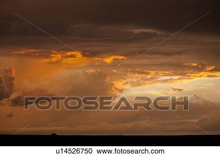 Stock Image - Dramatic orange grey swirling clouds of stormy sky on Mara plain with silhouetted safari jeep on black horizon, Masai Mara, Kenya, East Africa. Fotosearch
